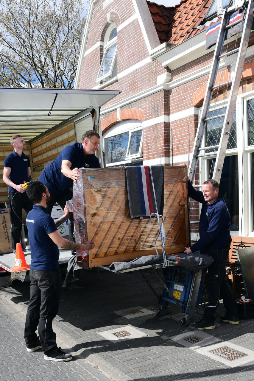 Verhuizers laden een piano op een dolly in een verhuiswagen via een laadklep.